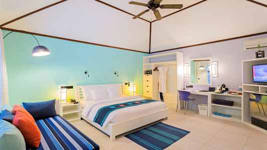 Et lyst hotelværelse med en dobbeltseng, farverig dekoration og en siddegruppe. (AI-genereret tekst)