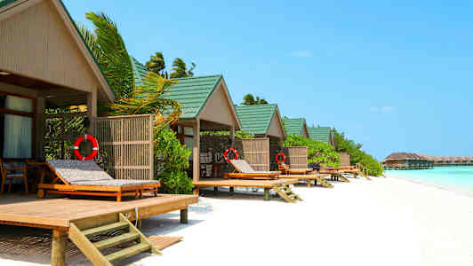 Strandbungalower med grønne tage og liggestole ved vandet. (AI-genereret tekst)