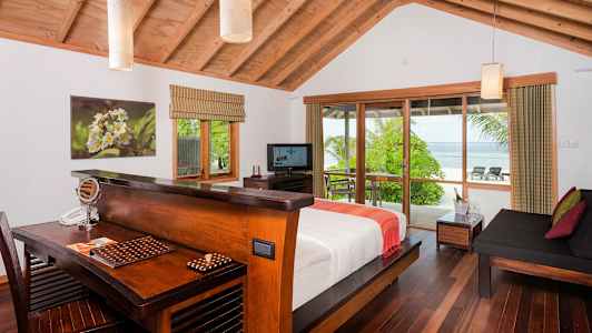 Et lyst hotelværelse med trædetaljer og udsigt over en frodig have og havet gennem store vinduer. (AI-genereret tekst)