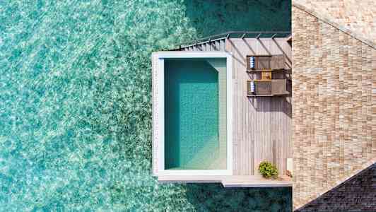 Et billede oppefra af et poolområde med trædæk ved vandet. (AI-genereret tekst)