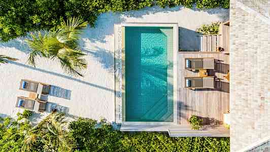 Luftfoto af en pool med omkringliggende træterrasse, liggestole og planter. (AI-genereret tekst)