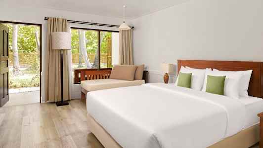 Et hotelværelse med en dobbeltseng, siddeplads og et vindue, der vender ud mod grønne træer. (AI-genereret tekst)