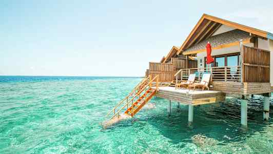 Fotografi af en bungalow på pæle over turkisvand. (AI-genereret tekst)