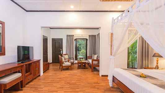 Et værelse med træmøbler, en seng med myggenet og en siddegruppe med udsigt til en have. (AI-genereret tekst)