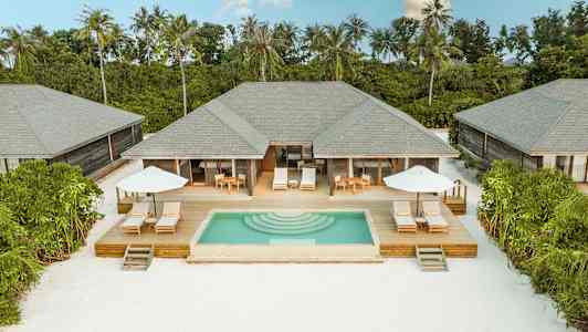 Villaer med private pools og solterrasser omgivet af grønt ved en hvid sandstrand. (AI-genereret tekst)