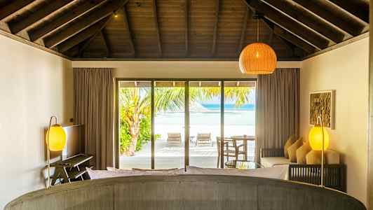 Rum med tagbjælker og udsigt til stranden gennem store glasdøre. (AI-genereret tekst)