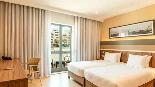 Hotelværelse med to enkeltsenge, skrivebord og en balkon med glasdøre. (AI-genereret tekst)