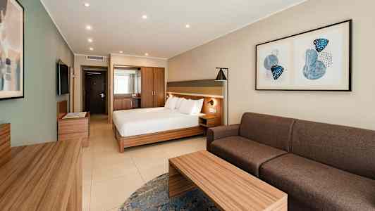 Et hotelværelse med en dobbeltseng, sofa, bord og vægkunst. (AI-genereret tekst)