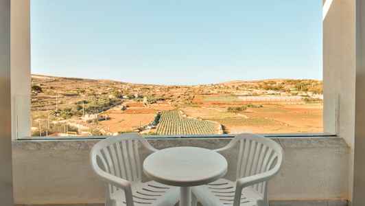 To hvide plastikstole og et rundt bord på en terrasse med udsigt over marker. (AI-genereret tekst)