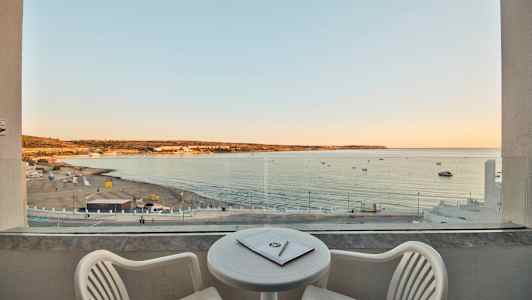 Udsigt fra en balkon over en sandstrand og havet ved solnedgang. (AI-genereret tekst)