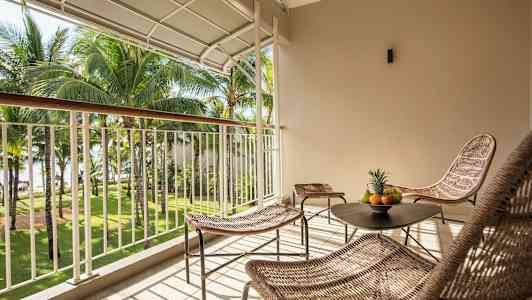 En møbleret balkon med udsigt over en have med palmer. (AI-genereret tekst)
