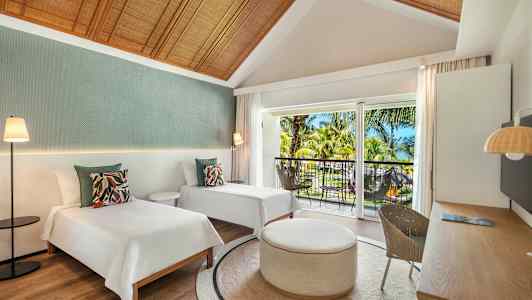 Et hotelværelse med to enkeltsenge, et rundt bord og en balkon med udsigt over tropiske træer. (AI-genereret tekst)