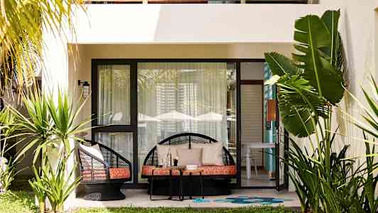 En terrasse med lænestole, bord og planter foran en bolig. (AI-genereret tekst)