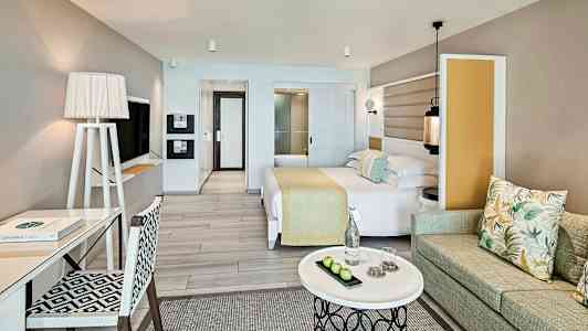 Et hotelværelse med moderne interiør, seng, skrivebord, sofa og et sofabord. (AI-genereret tekst)