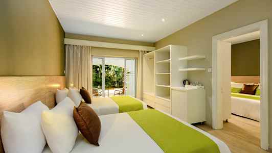 Hotelværelse med to senge, grønne sengetæpper og udsigt til haven. (AI-genereret tekst)