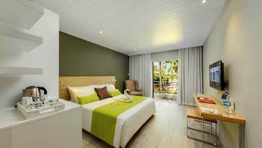 Hotelværelse med dobbeltseng, skrivebord og altan med udsigt til træer og grønt. (AI-genereret tekst)