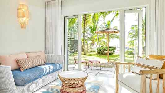 Stue med hvid sofa, blå pude og glasdøre, der åbner ud til en have med palmetræer. (AI-genereret tekst)