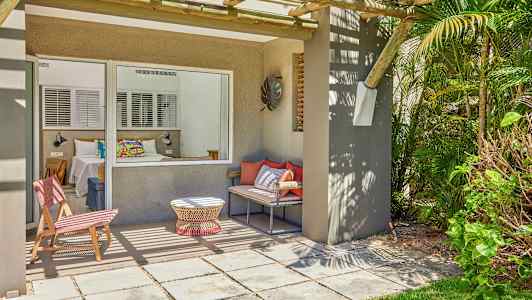 En terrasse med siddepladser og udsigt til et soveværelse gennem et stort vindue. (AI-genereret tekst)