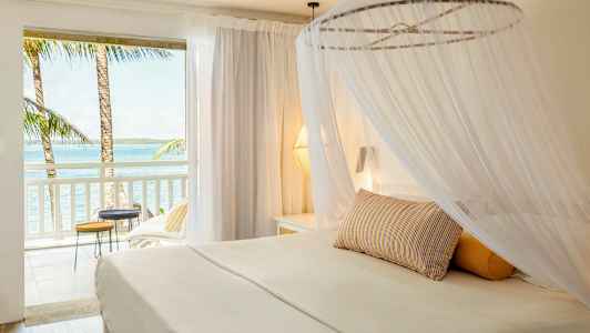 En lys hotelsuite med en himmelseng og udsigt over havet fra altanen. (AI-genereret tekst)