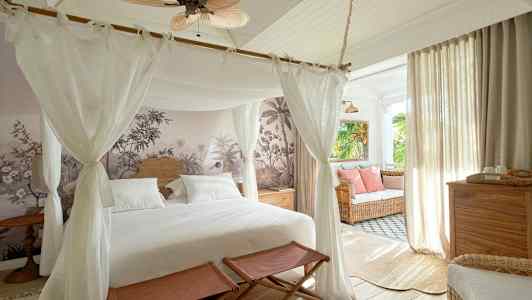 Et soveværelse med himmelseng, vægdekoration og indretning med lyse møbler samt en siddegruppe ved vinduet. (AI-genereret tekst)