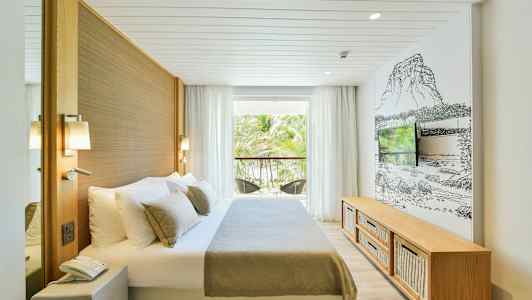 Et hotelværelse med en seng, et fjernsyn og en altan med udsigt til et område med palmetræer. (AI-genereret tekst)