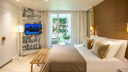 Hotelværelse med dobbeltseng, udendørs siddeplads ved døren og vægmonteret tv. (AI-genereret tekst)