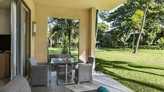 Udsigt fra en terrasse med havemøbler mod grønt område og palmer. (AI-genereret tekst)