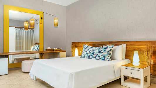 Et hotelværelse med en seng med dekorative puder, et natbord med en lampe og et stort spejl med gul ramme. (AI-genereret tekst)