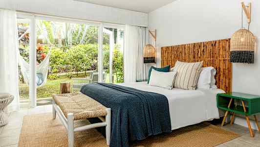 Et soveværelse med dobbeltseng, trædetaljer og store vinduer med udsigt til grønt. (AI-genereret tekst)