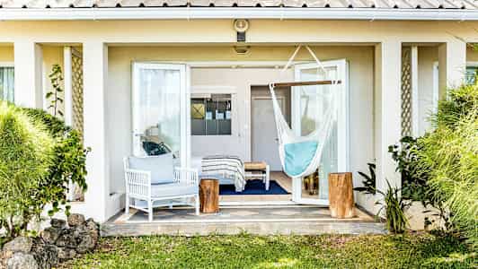 Billede af en terrasse med åben terrassedør, en hvid siddegruppe, en hængekøje og grønne planter omkring. (AI-genereret tekst)