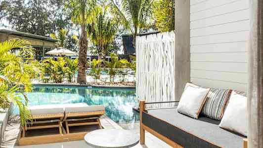 Udendørsområde med pool, solsenge og en sofa med puder. (AI-genereret tekst)