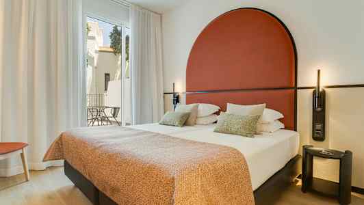 Moderne hotelværelse med dobbeltseng, rødt sengegærde og store vinduer mod en altan. (AI-genereret tekst)