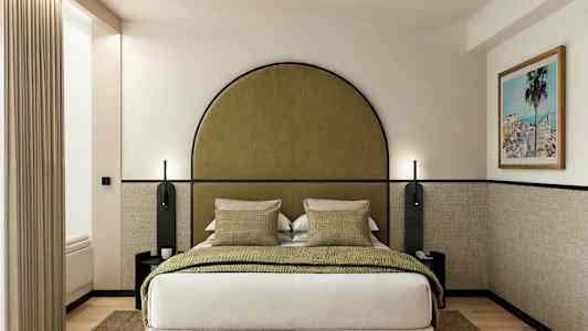 Et hotelværelse med en seng, grønne puder og et indrammet billede på væggen. (AI-genereret tekst)