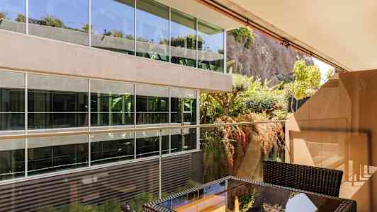 Udendørsområde med møbler foran en moderne glasbygning ved en grøn bevokset klippevæg. (AI-genereret tekst)