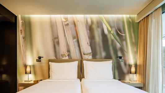 To enkeltsenge med hvide lagner foran en væg med bambusmotiv. (AI-genereret tekst)