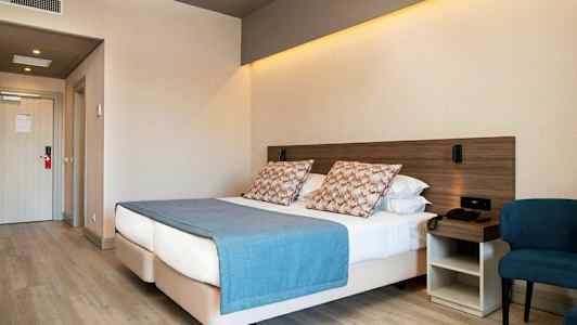 Hotelværelse med en dobbeltseng, blå sengelagen og puder, ved siden af en stol og et natbord. (AI-genereret tekst)