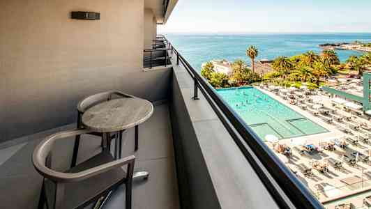 Altan med bord og stole med udsigt over en pool og havet. (AI-genereret tekst)