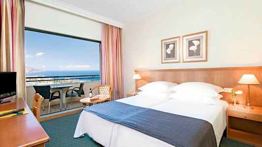 Hotelværelse med dobbeltseng, natbord og balkon med udsigt over havet. (AI-genereret tekst)