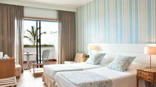 Et hotelværelse med to enkeltsenge, dekorative puder og en balkon med stole og bord. (AI-genereret tekst)