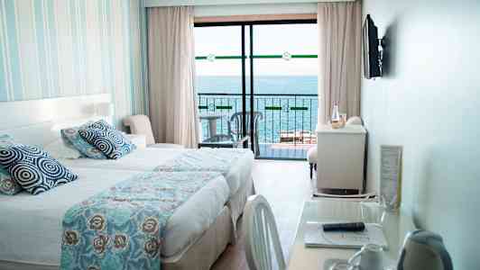 Et hotelværelse med en seng, et skrivebord og udsigt over havet fra en altan. (AI-genereret tekst)