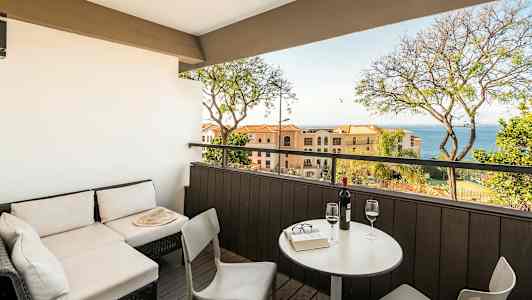 En terrasse med siddeområde og udsigt mod havet, med bord og to glas vin. (AI-genereret tekst)