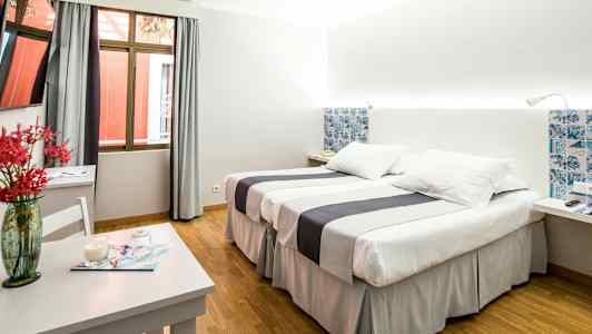 Hotelværelse med to senge, et bord med dekorativ vase og et vindue. (AI-genereret tekst)