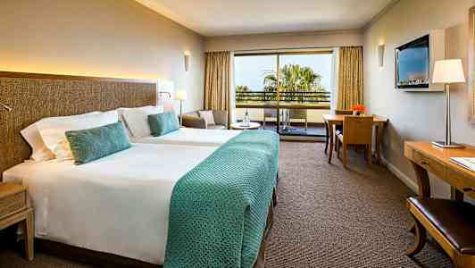 Et hotelværelse med to enkeltsenge, en siddegruppe, et skrivebord og en balkon med udsigt. (AI-genereret tekst)