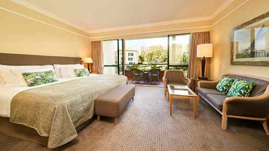 Hotelværelse med stor seng, siddeområde og altan med udsigt. (AI-genereret tekst)