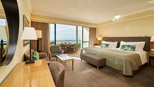 Et hotelværelse med seng, siddeområde og udsigt til altan og hav. (AI-genereret tekst)