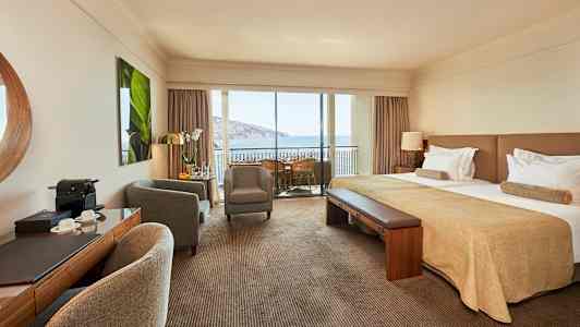 Hotelværelse med dobbeltseng, siddeområde og balkon med udsigt over havet. (AI-genereret tekst)