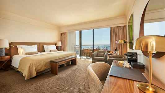 Et stilfuldt hotelværelse med en dobbeltseng, skrivebord og siddesektion samt store vinduer mod en balkon. (AI-genereret tekst)