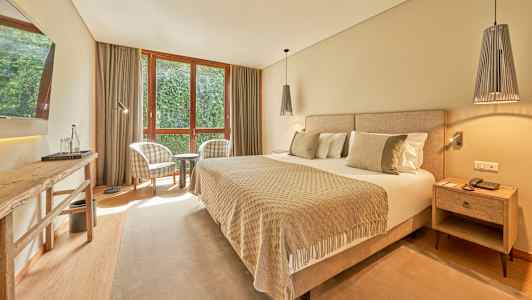 Et hotelværelse med en bred seng, to lænestole ved et vindue og et bord. (AI-genereret tekst)