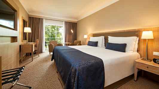 Hotelværelse med dobbeltseng, siddeområde, skrivebord og udsigt til grønne omgivelser. (AI-genereret tekst)