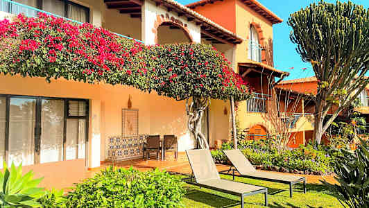 En bygning med blomsterudsmykninger, grøntområder og liggestole på en græsplæne. (AI-genereret tekst)